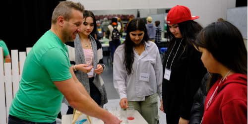 Volunteer working with four students at a Career Expo station on strawberry DNA